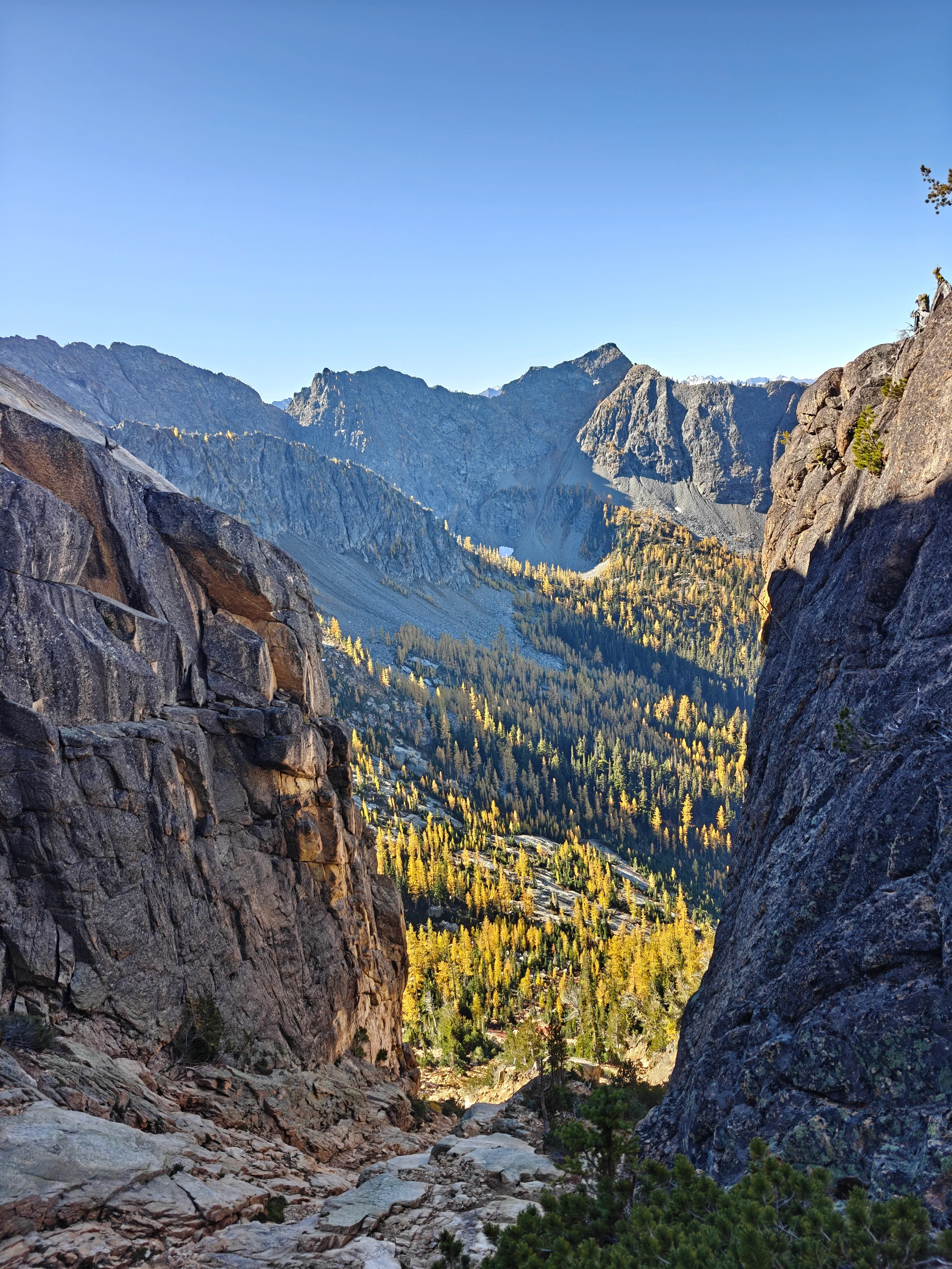 View down a rocky gully between granite walls to a valley full of golden larches