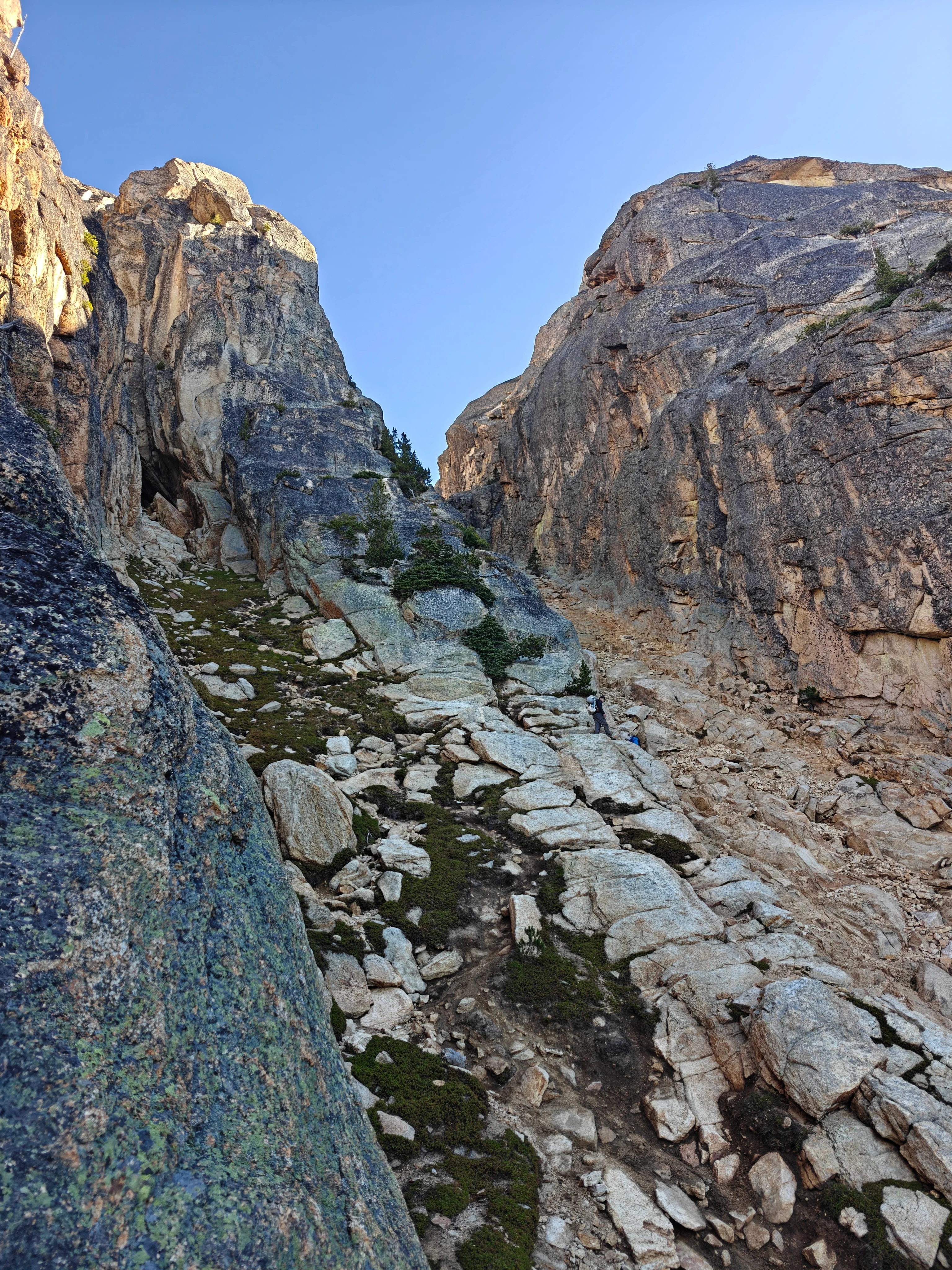 Looking up a steep granite gully with a small climber partway up the talus and slabs