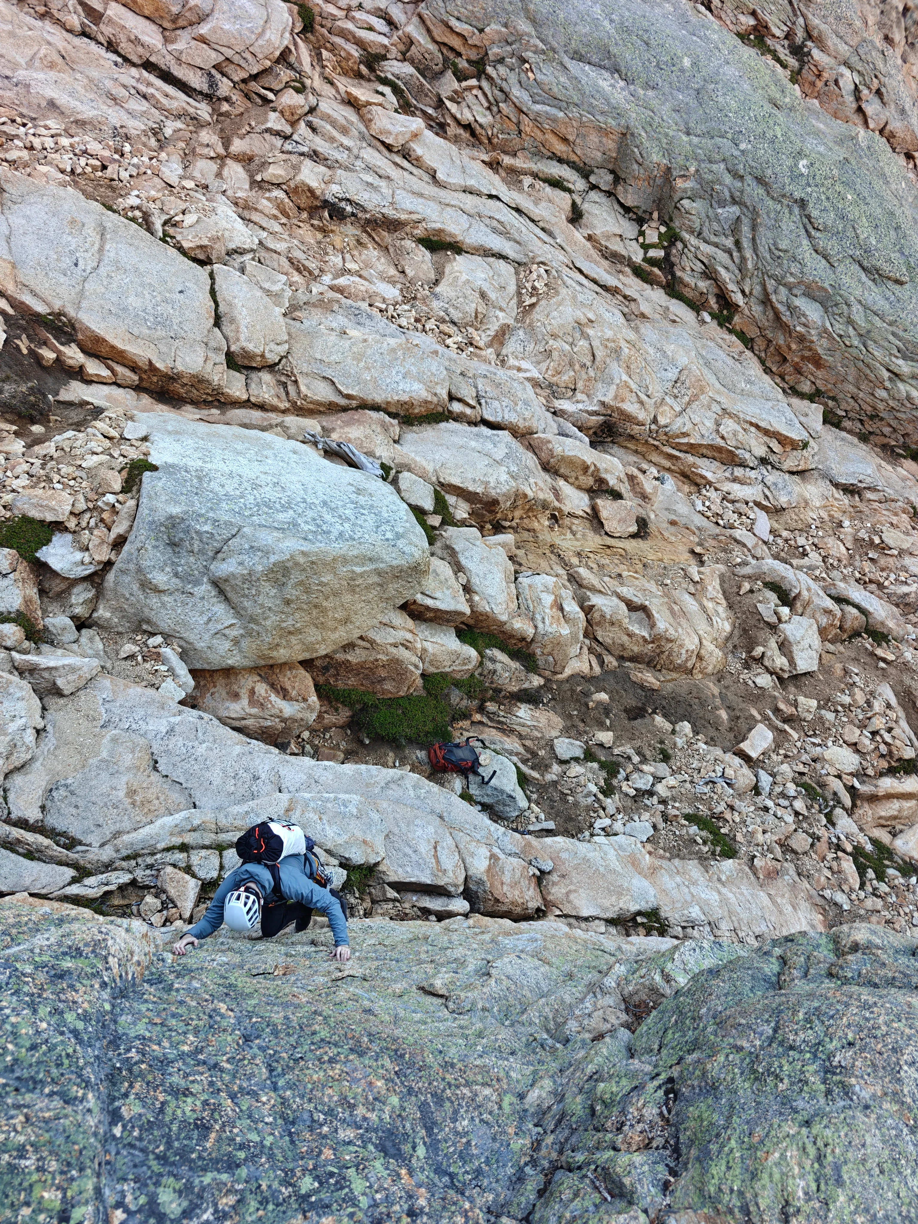 Climber in a white helmet scrambling up a lichen-covered slab in the gully
