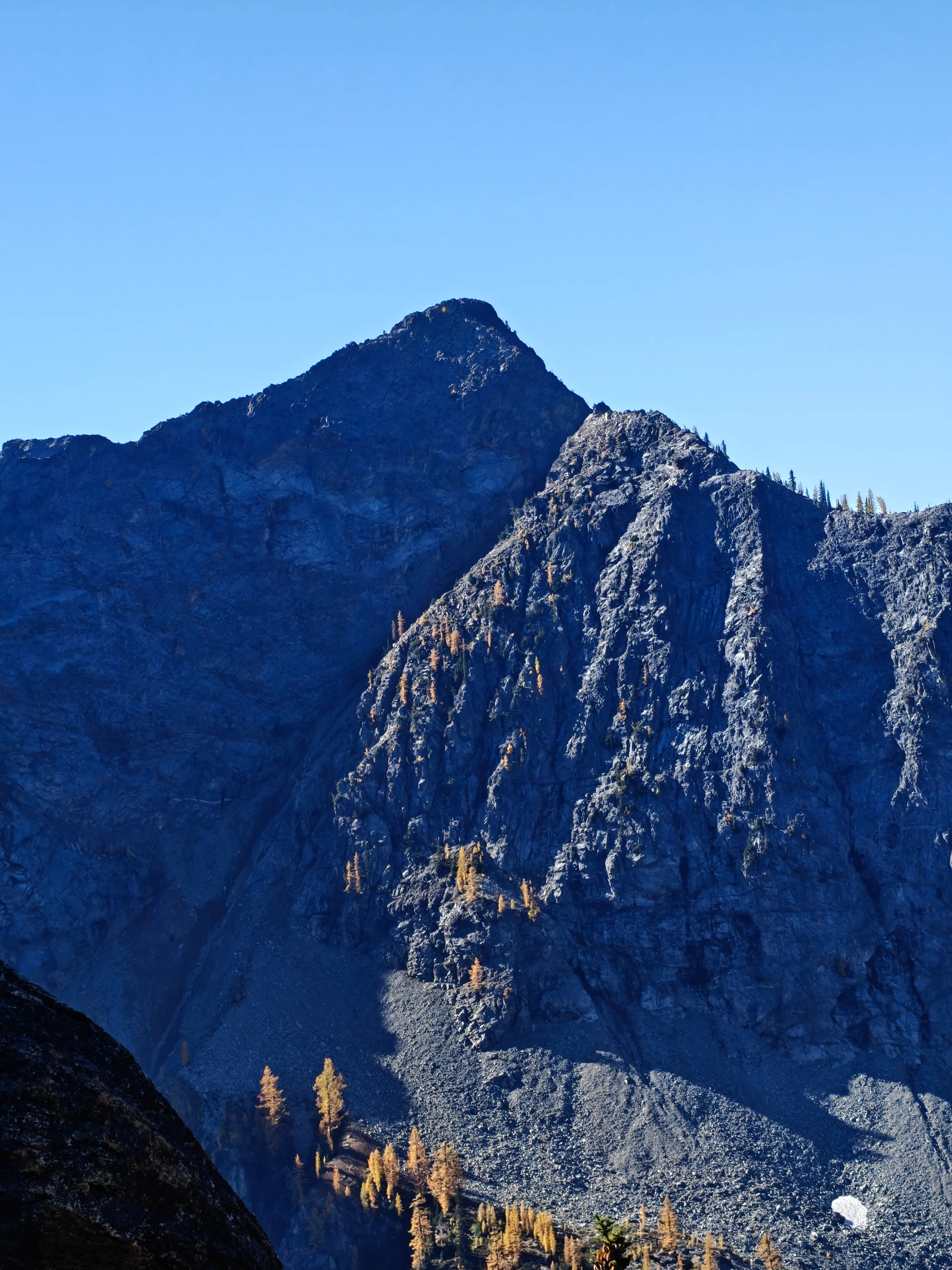 Shaded rocky peak across the cirque with scattered golden larches and talus below
