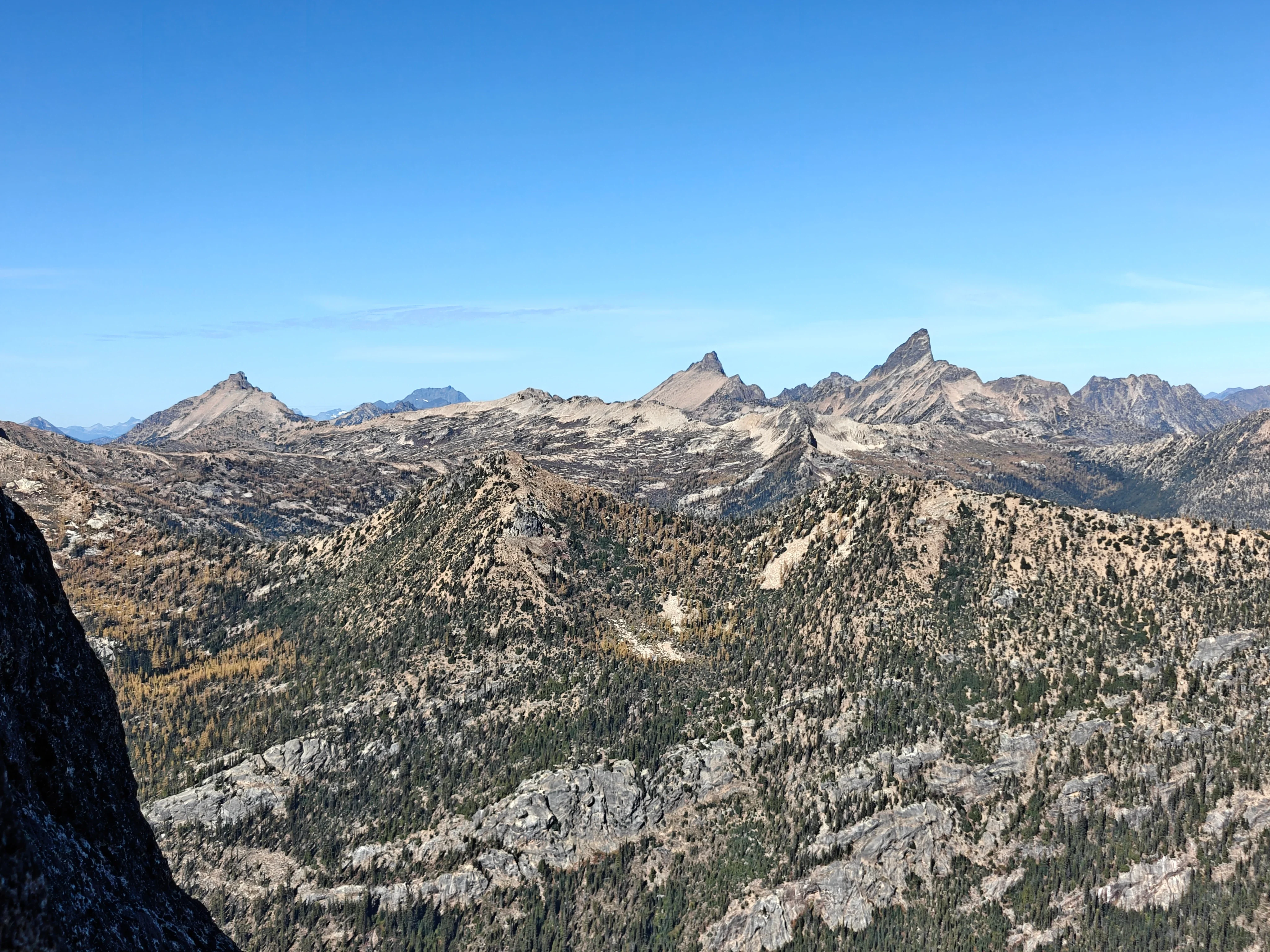 Panorama from the face of jagged granite peaks and forested ridges stretching to the horizon