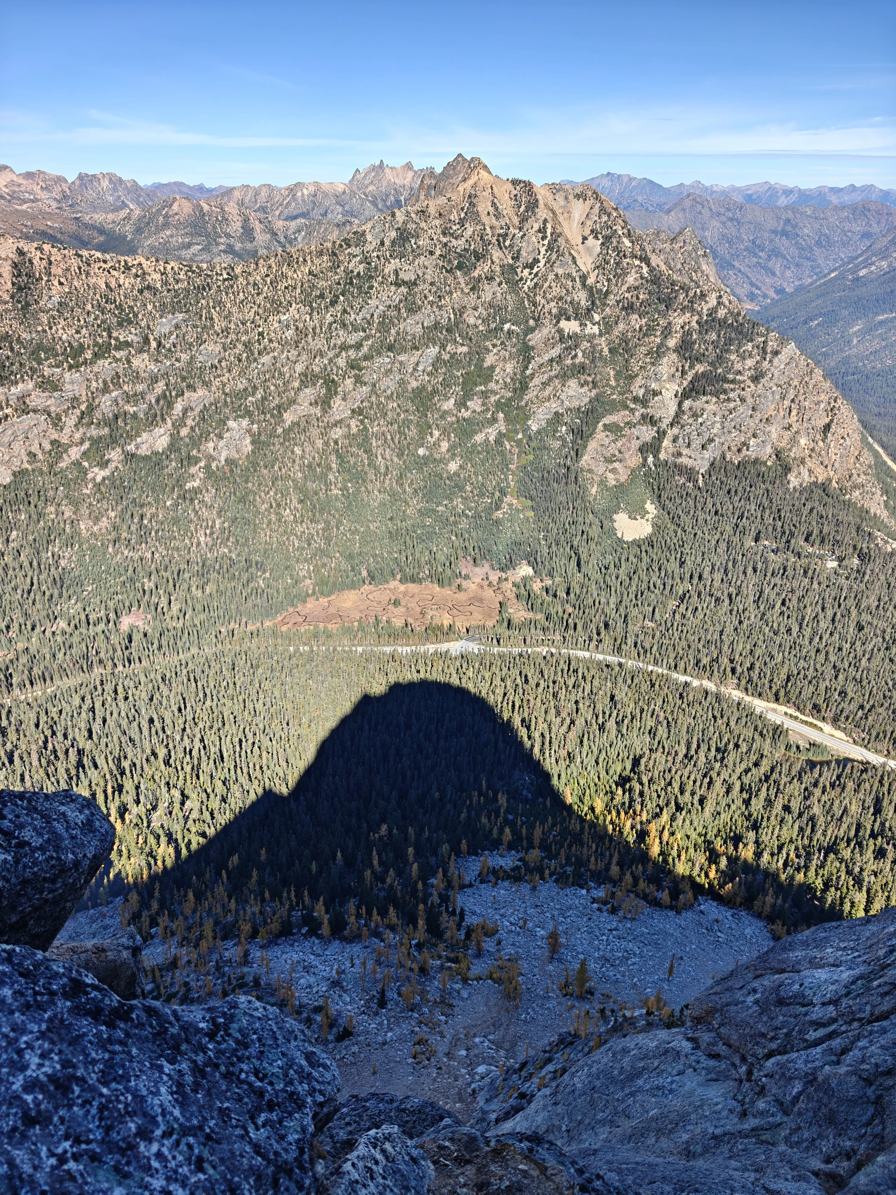 The shadow of the peak cast across the forest and talus far below, with the highway curving through the valley
