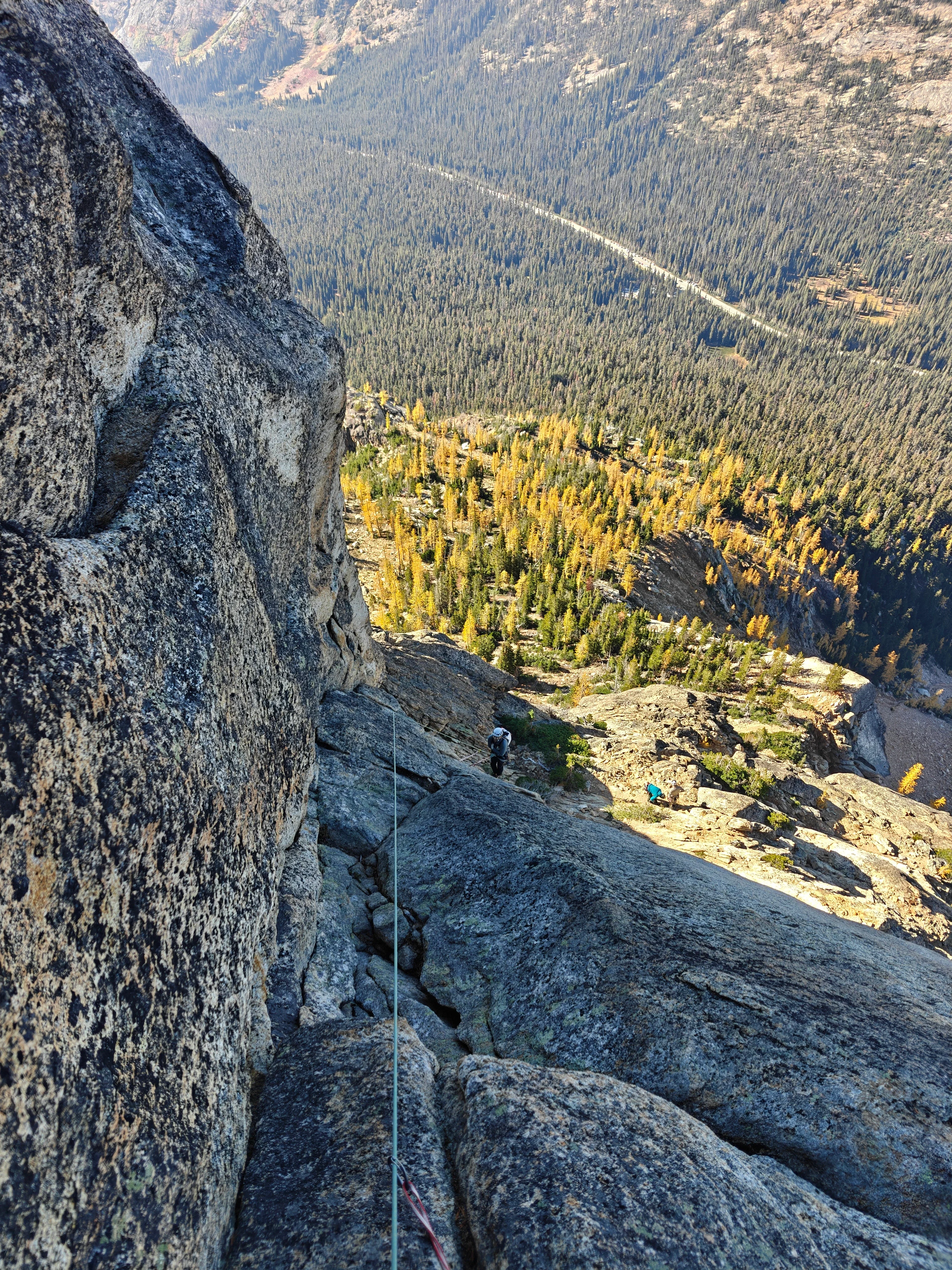 Looking down the rope at climbers on the lower face, golden larches and the highway valley far below