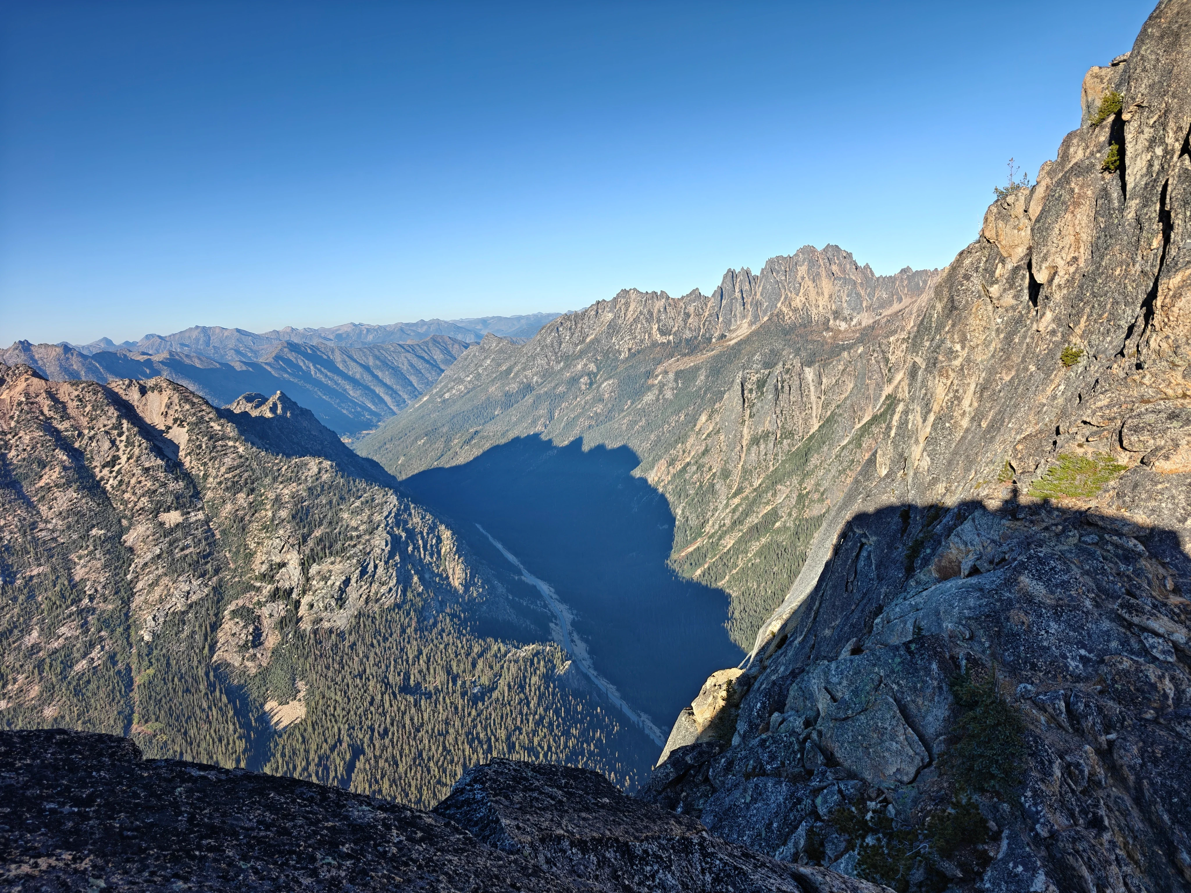 Evening view from high on the mountain down a long valley filling with shadow, jagged ridgeline on the right