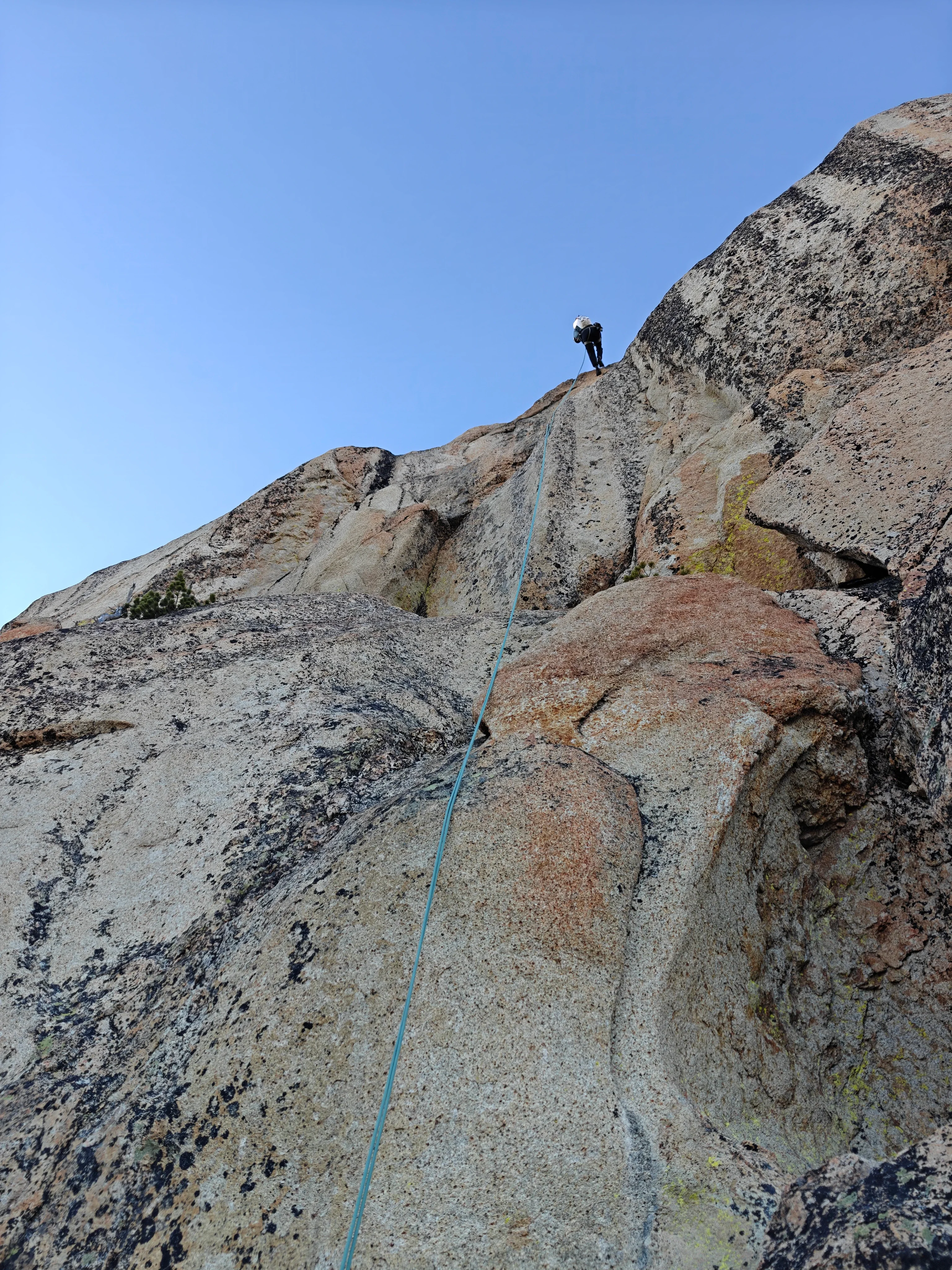 Climber rappelling over the edge of a tan granite slab, rope running down toward the camera
